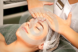 Head massage. Beautiful caucasian young white woman receiving a head and forehead massage with closed eyes in a spa