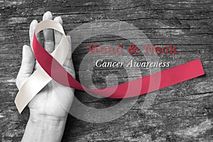 Head and neck cancer awareness with symbolic burgundy ivory white ribbon on hand and old aged wood photo