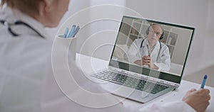 Head physician of hospital is communicating with doctors by video conference, woman is listing him and making notes