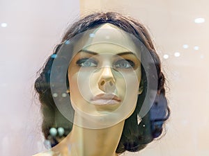 Head of realistic female mannequin behind glass of shop window