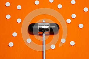 Head of reflex hammer is on orange background surrounded by pills or tablets with ornament of polka dots. Concept photo diagnosis,