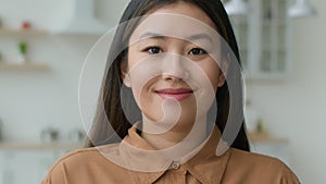 Head shot of Asian woman with natural makeup posing in home kitchen Korean Japanese businesswoman looking at camera