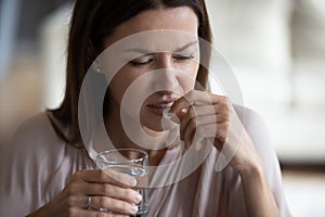 Head shot close up unhealthy young woman taking painkiller.