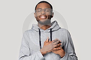 Head shot grateful African American man holding hands on chest