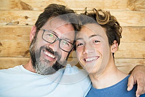 Head shot happy teenager son embracing shoulders of happy middle aged father, looking at camera. Positive two male generations