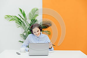 Head shot happy young indian ethnicity female manager wearing wireless headphones, looking at laptop screen,