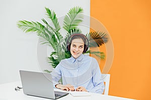 Head shot happy young indian ethnicity female manager wearing wireless headphones, looking at laptop screen,