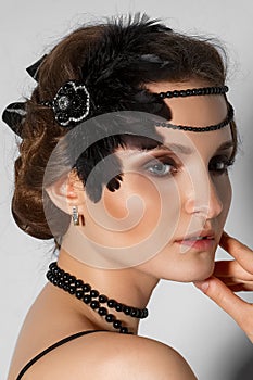 Head shot of model with plume in hair and black pearl bead in profile