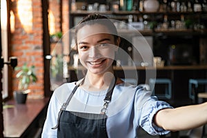 Head shot portrait of attractive smiling waitress in cozy coffeehouse