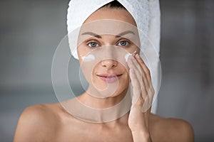 Head shot portrait beautiful woman applying cream on cheekbones