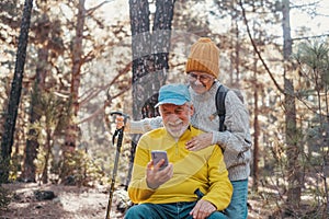 Head shot portrait close up of couple of cute seniors using phone together in the forest with trees around them. Using cellphone