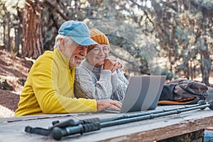 Head shot portrait close up of cute couple of old middle age people using computer pc outdoors sitting at a wooden table in the