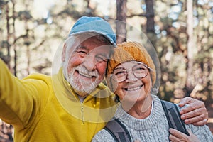 Head shot portrait close up of cute couple of old seniors taking a selfie together in the mountain forest looking at the camera