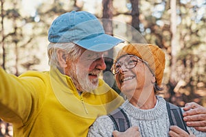 Head shot portrait close up of cute couple of old seniors taking a selfie together in the mountain forest looking at the camera