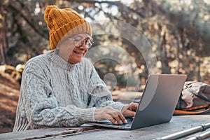 Head shot portrait close up of cute one of old middle age person using computer pc outdoors sitting at a wooden table in the