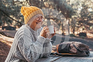 Head shot portrait close up of middle age woman relaxing drinking coffee or tea sitting at table in the forest of mountain in the