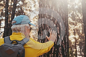 Head shot portrait close up of one old cute man touching big tree in the forest of mountain in the nature taking care. One mature