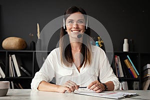 Head shot portrait confident businesswoman looking at camera and talking by headphones.