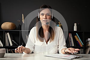 Head shot portrait confident businesswoman looking at camera and talking by headphones.