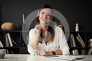 Head shot portrait confident businesswoman looking at camera and talking by headphones.