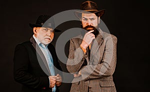 Head shot portrait of elderly mature dad and grownup son. Two male generations family. Men in hat on dark studio