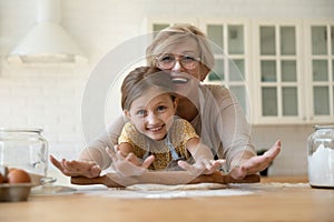 Head shot portrait happy grandmother with granddaughter rolling dough together