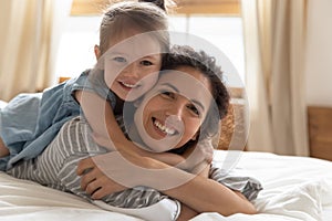 Head shot portrait little girl lying on happy mother back