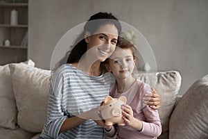 Head shot portrait mother and little daughter holding piggy bank