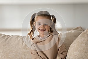 Head shot portrait of smiling 7s girl sitting on couch