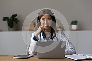 Head shot portrait smiling female doctor in headphones using laptop