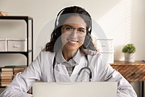 Head shot portrait smiling female doctor wearing headphones working online