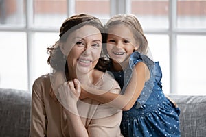 Head shot portrait smiling little girl hugging grandmother from back