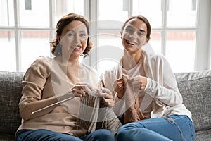 Head shot portrait smiling mature mother and grownup daughter knitting