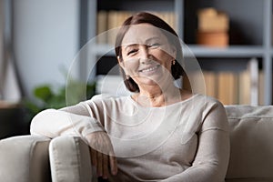 Head shot portrait smiling mature woman sitting on cozy couch