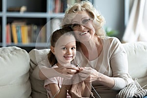 Head shot portrait smiling mature woman teaching little girl knitting