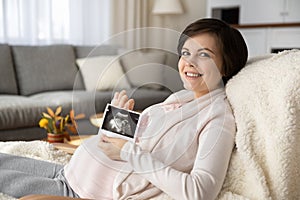 Head shot portrait of smiling pregnant woman showing ultrasound picture