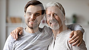 Head shot portrait smiling young man with mature father hugging