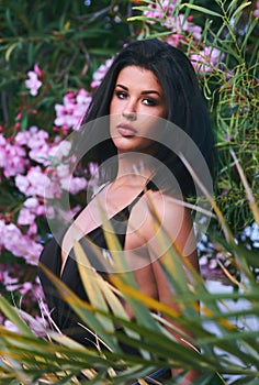 Head shot portrait of young brunette woman with bob hairstyle posing outdoors. Girl pose near blooming bright flowers