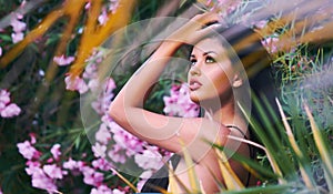 Head shot portrait of young brunette woman posing outdoors. Girl pose near blooming bright beautiful pink flowers and leaves