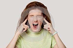 Head shot portrait young woman sticking plugging fingers in ears.