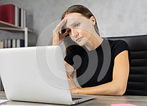 Head shot serious Caucasian businesswoman tired and touch head while working with computer, book shelf and copy space at