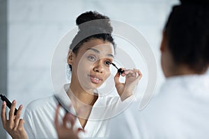 Head shot smiling African American woman applying mascara on eyelashes