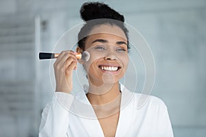 Head shot smiling African American woman using cosmetics brush