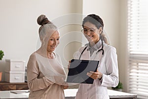 Head shot smiling doctor consulting mature patient, holding clipboard