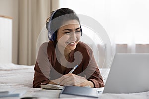 Head shot smiling Indian woman in headphones studying in bedroom