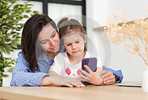 Head shot smiling young mother showing funny cartoons to overjoyed little adorable girl on smartphone.