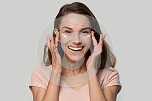 Happy woman looking at camera applying eyelid moisturizing cream photo