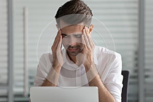 Head shot unhappy young male employee suffering from strong headache.