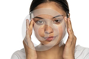 Head shot of a young beautiful woman applies concealer under her eyes
