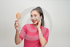 Head shot of young woman holding mirror and touching her face